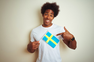 Young afro american man holding Sweden Swedish flag standing over isolated white background very happy pointing with hand and finger