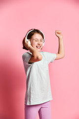 Fototapeta na wymiar Full-length amateur girl of music listens in white headphones, enjoying the pleasure of listening to music against a pink background