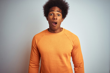 Fototapeta na wymiar Young american man with afro hair wearing orange sweater over isolated white background afraid and shocked with surprise expression, fear and excited face.