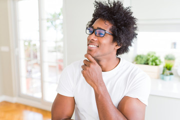 African American man wearing glasses with hand on chin thinking about question, pensive expression. Smiling with thoughtful face. Doubt concept.