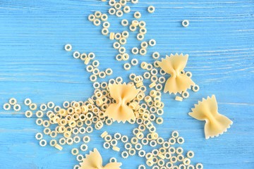 Traditional italian farfalle pasta and tiny round noodles with selective focus on blue textured wood background. Bow tie noodles with small rings pasta on wood backdrop. Raw organic noodles. Uncooked