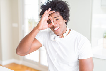 African American man wearing headphones listening to music doing ok gesture with hand smiling, eye looking through fingers with happy face.