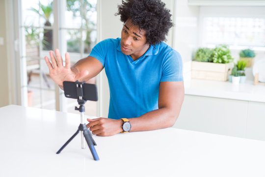 African American man doing online call with webcam using smartphone with open hand doing stop sign with serious and confident expression, defense gesture