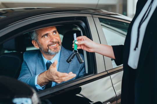saleswoman giving car keys to a customer in car dealership showroom