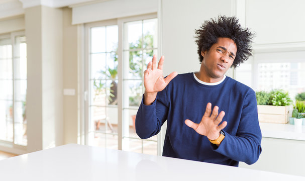 Young african american man wearing casual sweater sitting at home disgusted expression, displeased and fearful doing disgust face because aversion reaction. With hands raised. Annoying concept.