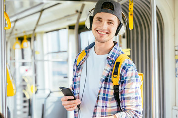 Young man is standing in a bus with headset on his head and listening to the music.