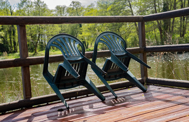 Two green plastic chairs leant against the wooden balustrade of the wooden pontoon overlooking a...