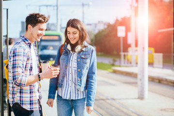 Young happy laughing couple standing on tram stop in sunny summer day.