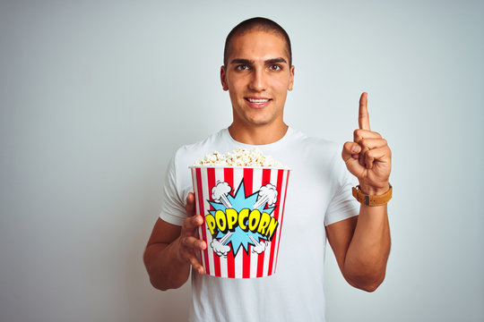 Young handsome man eating popcorn over white isolated background surprised with an idea or question pointing finger with happy face, number one