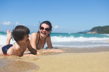 Fototapeta premium Mom with the small son On beach in the sea waves. Happy family enjoy at beach. Summer vacation, smiling and joy in waves