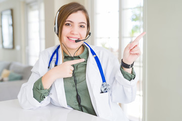 Beautiful young doctor woman wearing headset smiling and looking at the camera pointing with two hands and fingers to the side.