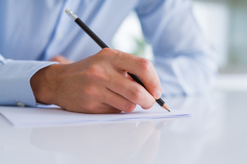 Close up of man hands writing using a pencil on paper over white table