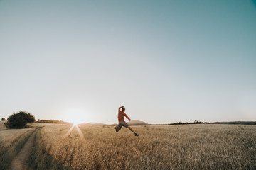 Young boy jumping in a wheat field at sunset next to the sun's rays
