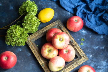 Still life of an old grandmother’s photo frame, apples, a tea pot with a cup of tea and an old metal candlestick. From the back, blue fabric on a dark background. 