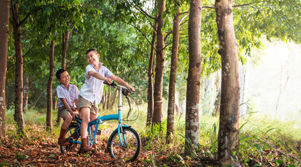 Fototapeta premium kids riding bike in rural thailand; Children playing in rice field countryside of asia.