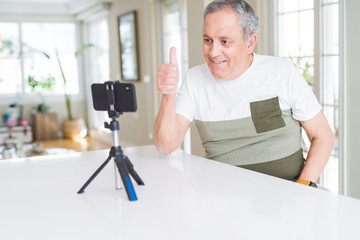 Handsome senior man doing video conference talking to the smartphone camera doing happy thumbs up gesture with hand. Approving expression looking at the camera with showing success.