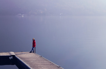Young girl sitting on the pier on lake and mountains background.