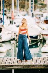 Outdoor fashion portrait of beautiful young woman posing by the lake, wearing red and white stripe...