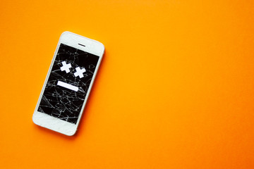 Broken smartphone with cracked destroyed screen on orange background with sad smile. Broken phone...