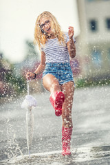 Cheerful girl jumping with white umbrella in dotted red galoshes. Hot summer day after the rain woman jumping and splashing in puddle