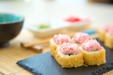 Hot fried Sushi Roll with cream cheese on black stone on bamboo mat decorated. Japanese cuisine Healthy and tasty food.