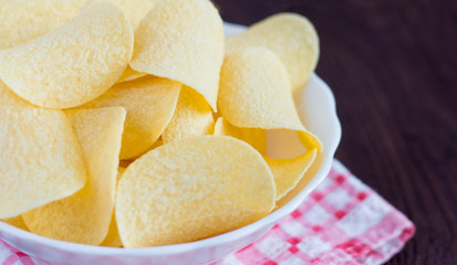 a full bowl of delicious potato chips on a wooden table,close-up