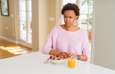 Young african american woman having healthy breakfast in the morning at home skeptic and nervous,...