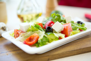 Fresh Greek salad on a plate on wooden cutting board Healthy and tasty food.