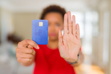 Young african american woman holding credit card with open hand doing stop sign with serious and...