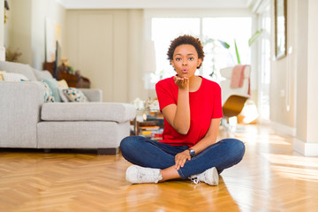 Young beautiful african american woman sitting on the floor at home looking at the camera blowing a kiss with hand on air being lovely and sexy. Love expression.