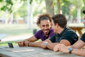 happy young men smiling and pointing at the smartphone at a park picnic table