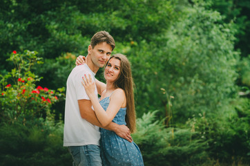Beautiful couple in bright clothes walks in a summer park in the city. Walk in the fresh air. Date of two lovers. The period of courtship of a man for a woman, romantic meetings in nature