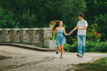 Obraz premium Beautiful couple in bright clothes walks in a summer park in the city. Walk in the fresh air. Date of two lovers. The period of courtship of a man for a woman, romantic meetings in nature