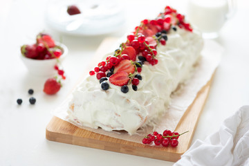 Sponge (biscuit) cake roll filling whipped cream and berries decorated strawberry, blueberry and red currants on white wooden background. Soft focus. Summer food concept