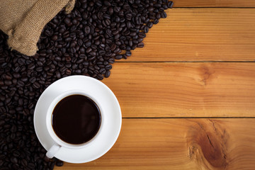 cup of coffee and coffee beans in a sack on wood background, top view.