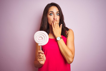 Young beautiful woman eating sweet candy over pink isolated background cover mouth with hand shocked with shame for mistake, expression of fear, scared in silence, secret concept