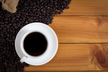 cup of coffee and coffee beans in a sack on wood background, top view.
