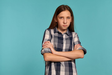 Beautiful teenage girl in a casual checkered shirt is posing against a blue studio background.
