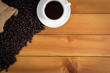 cup of coffee and coffee beans in a sack on wood background, top view.