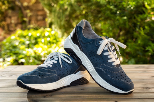 Close-up of elegant light blue sports shoes in natural nubuck leather for adult men photographed outdoors on a vintage wooden table. Fashion accessories.