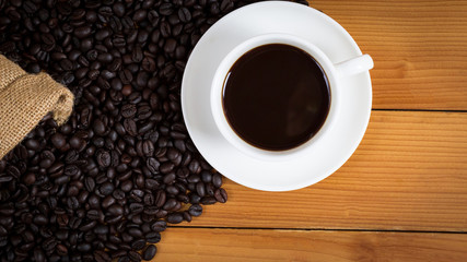 cup of coffee and coffee beans in a sack on wood background, top view.