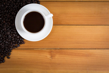 Cup of coffee and coffee beans on wood background, top view.