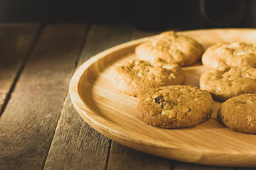 Oatmeal raisin cookies and wooden plate on wood background, dark food concept. Dessert with coffee and morning light.