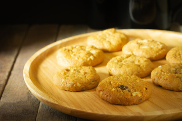 Oatmeal raisin cookies and wooden plate on wood background, dark food concept. Dessert with coffee and morning light.