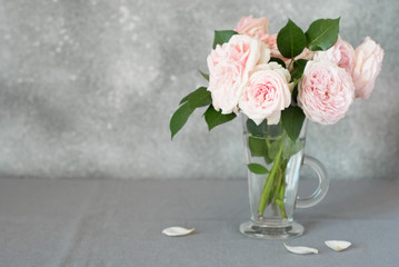 Tea roses in a glass on a table with a gray linen tablecloth. Still life. Copy space.