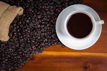 cup of coffee and coffee beans in a sack on wood background, top view.