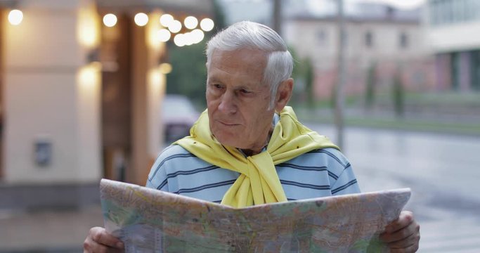 Senior male tourist exploring town with a map in hands and looking for the route