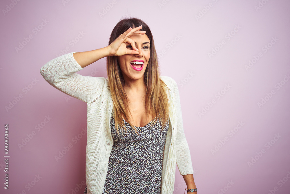 Wall mural young beautiful woman standing over pink isolated background doing ok gesture with hand smiling, eye