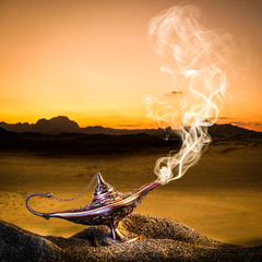 classic gold-colored aladdin lamp laid on the sand of a dune with smoke coming out.