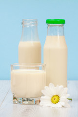 Two bottles and glass of milk in blue background.